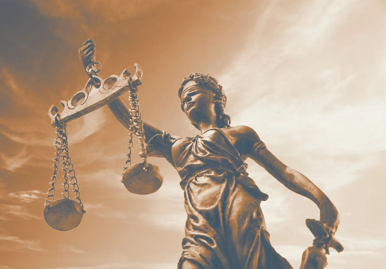 Lady Justice bronze statue holding balanced scales against a dramatic sky in warm sepia tone