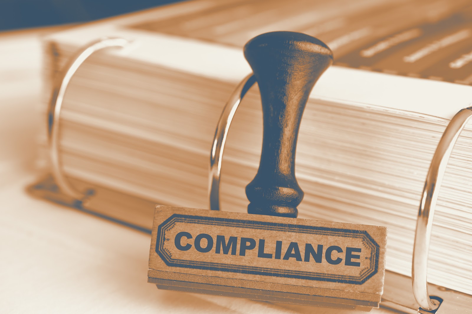 Wooden rubber stamp reading Compliance leaning against a ring binder with documents