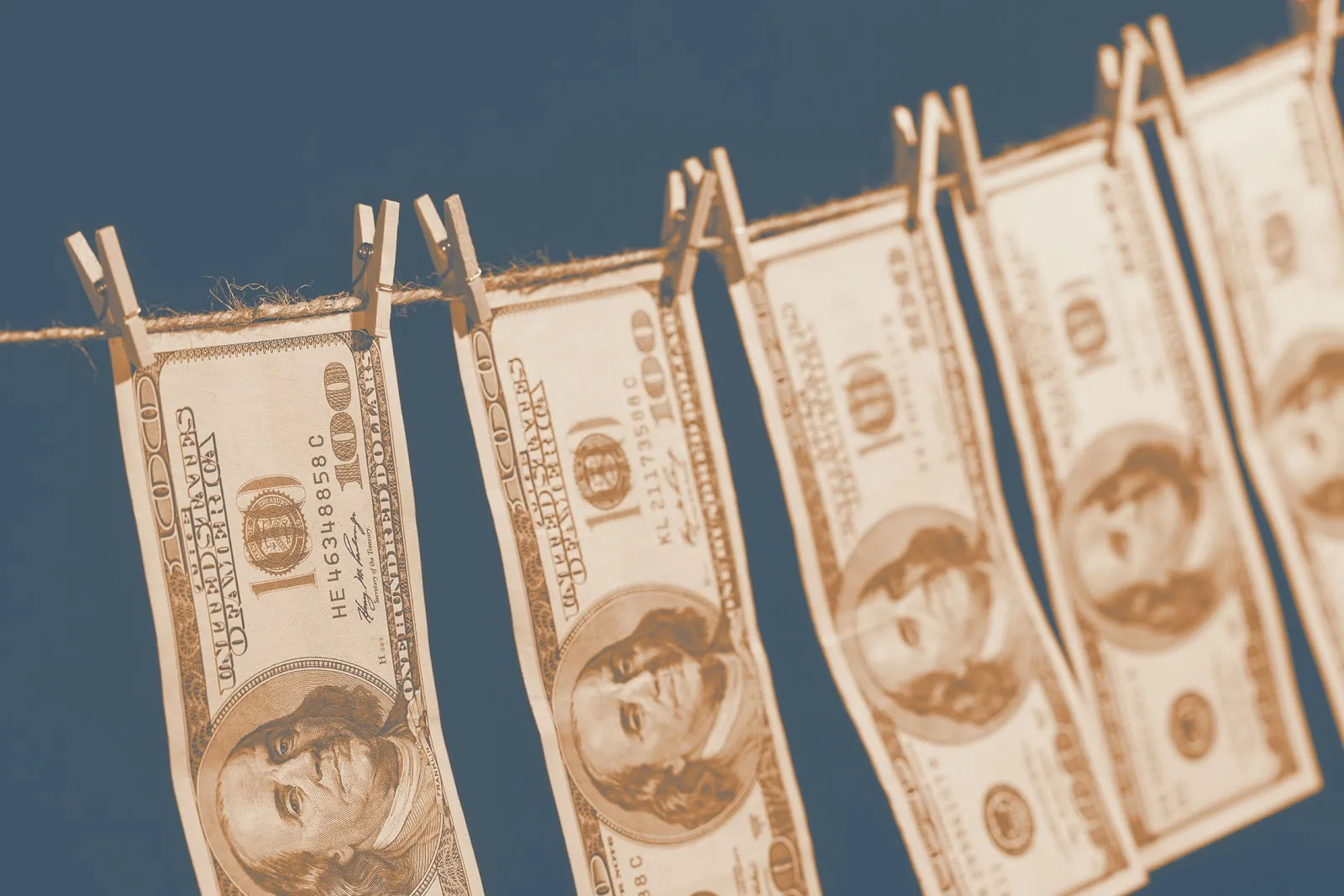 Hundred dollar bills hanging on a clothesline with wooden clothespins against a dark teal background