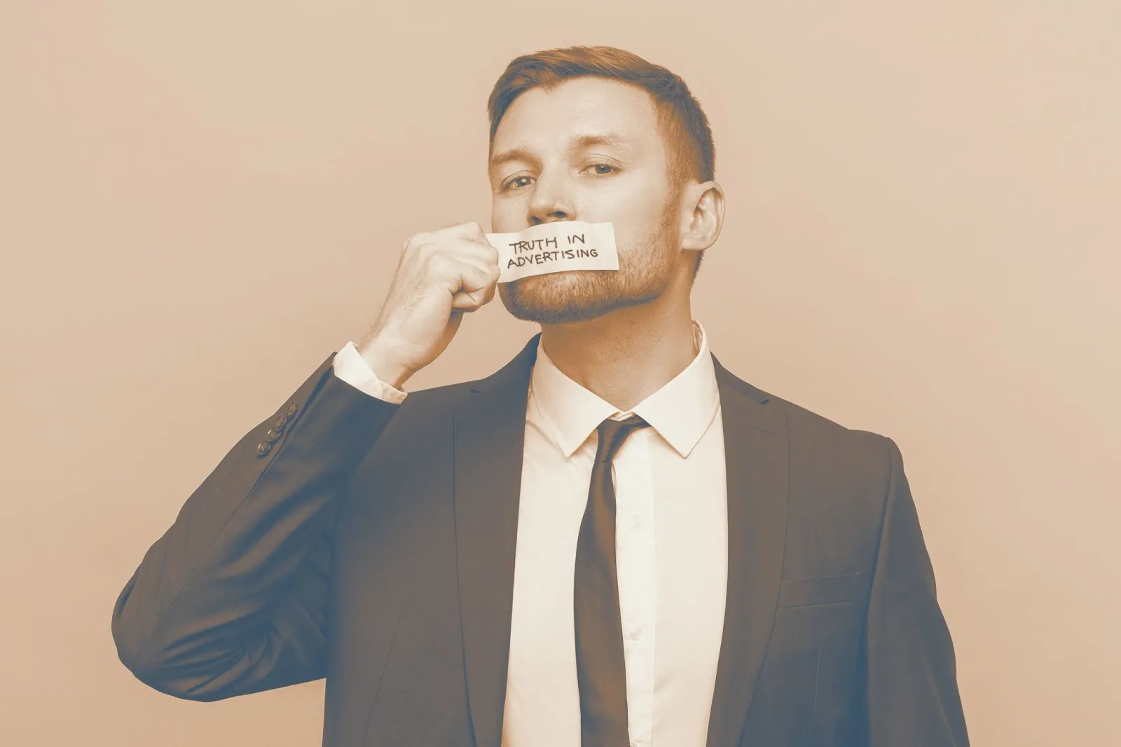 Businessman in suit holding a note reading Truth in Advertising over his mouth
