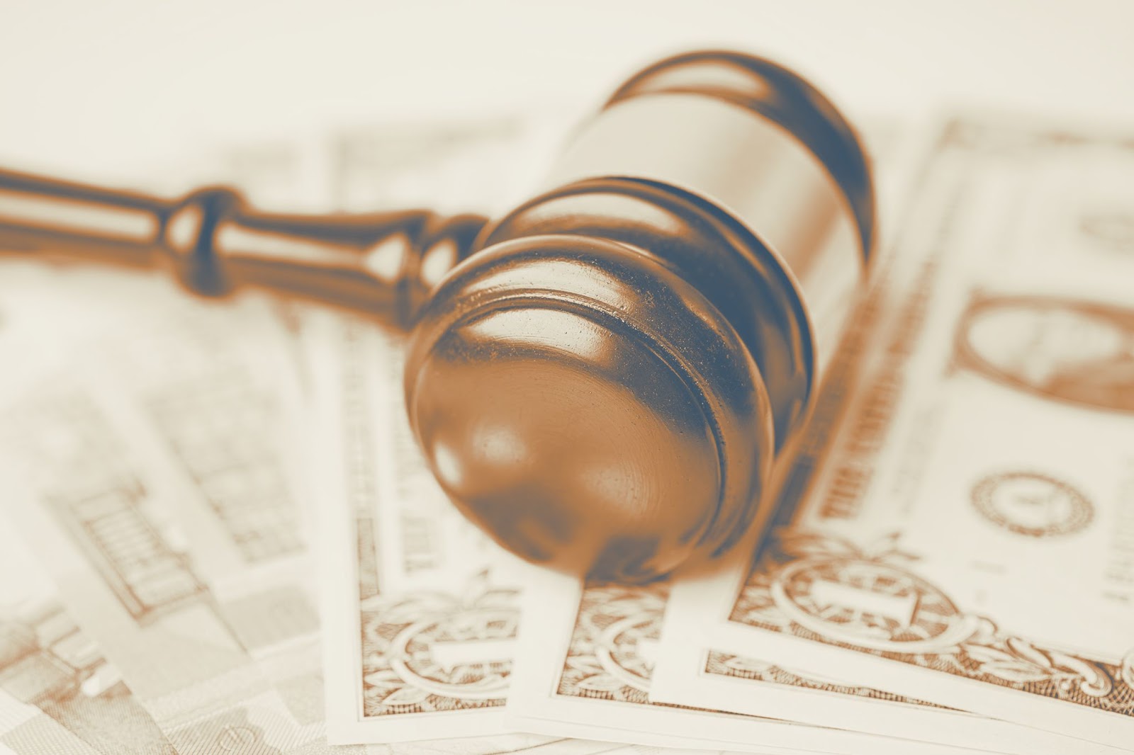 Wooden judges gavel resting on spread-out US dollar bills symbolizing financial penalties