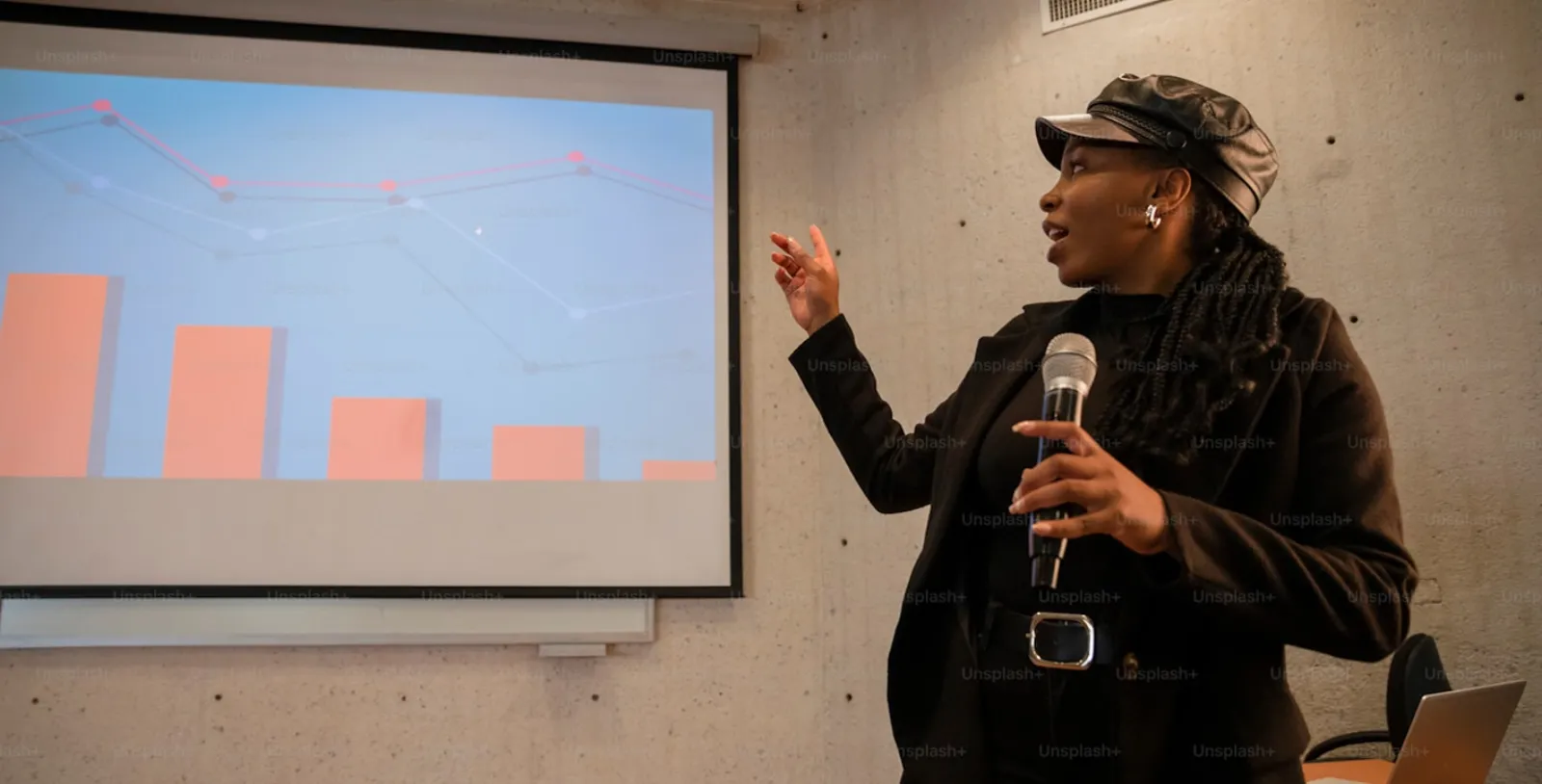 Speaker presenting bar charts and line graphs on a projector screen while holding a microphone